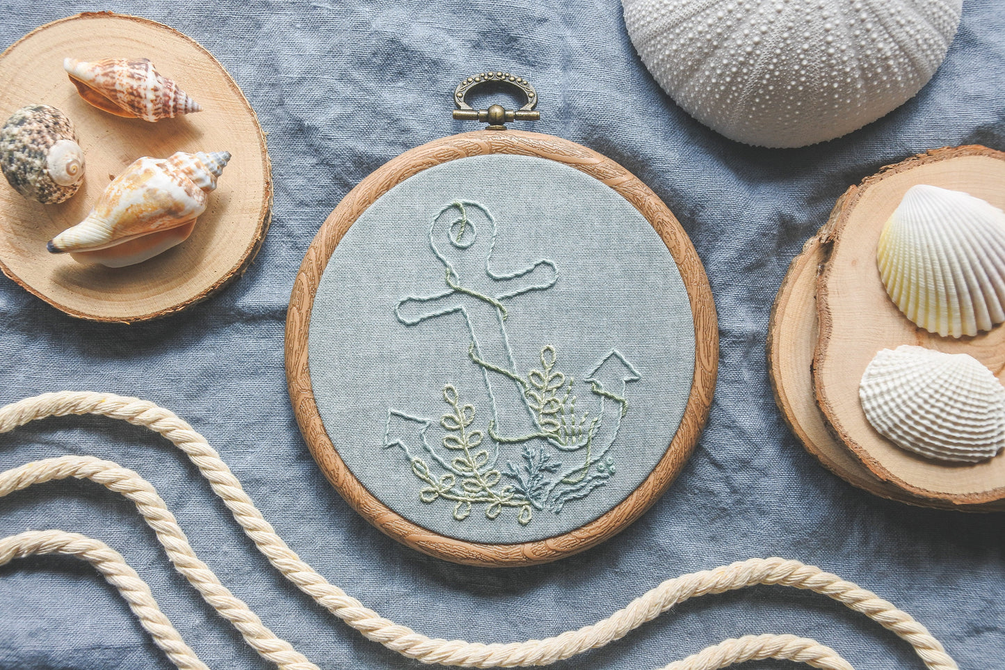 Flatlay of underwater anchor embroidery displayed with seashells and wave-like rope props on a blue fabric background