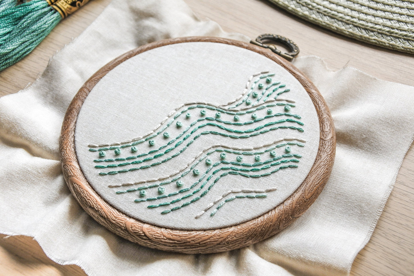 Angled closeup of turquoise and white backstitch and French knots in the beach wave embroidery pattern