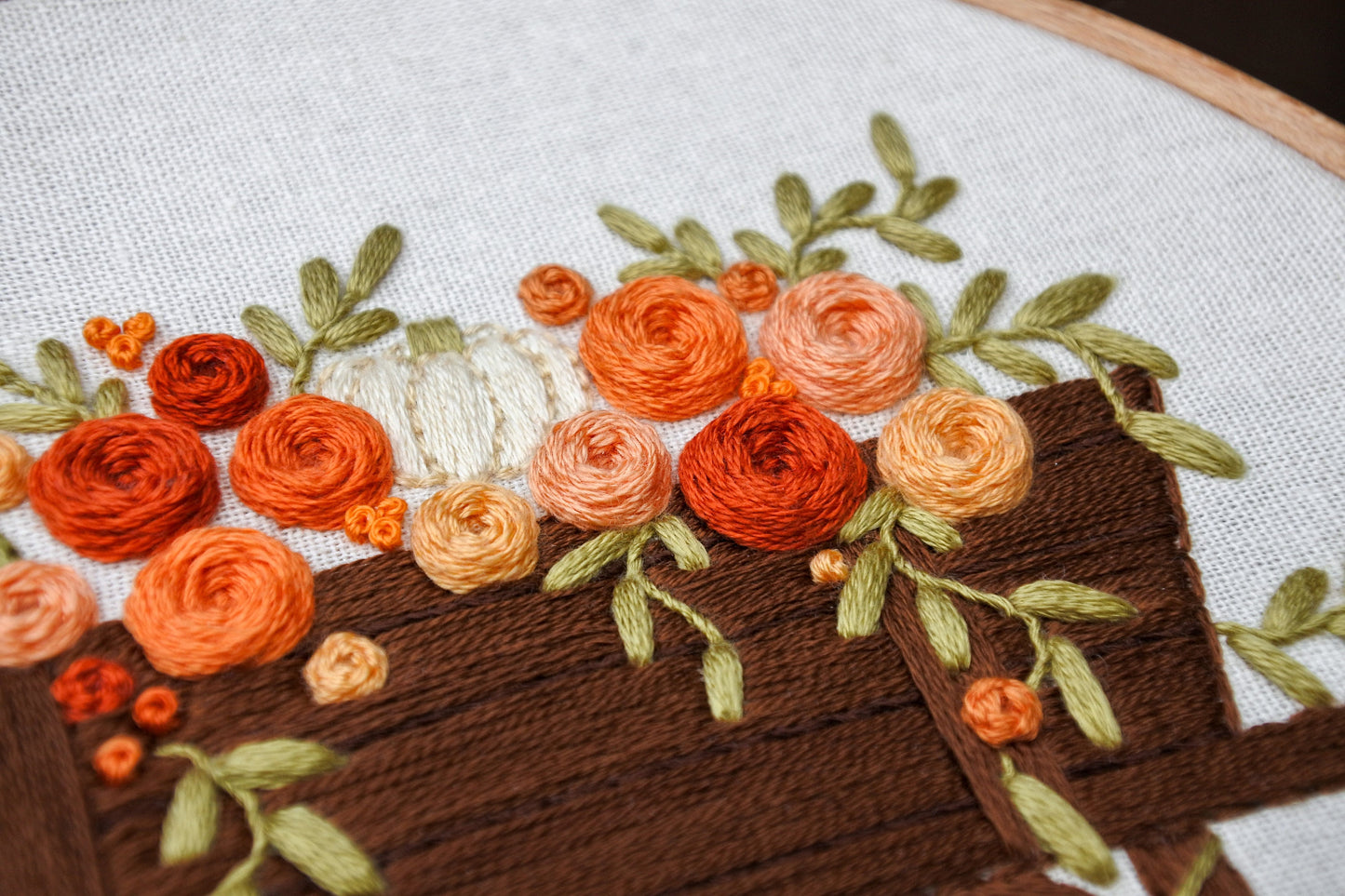angled closeup of hand embroidered pumpkin and flower details in the autumnal rustic wagon design