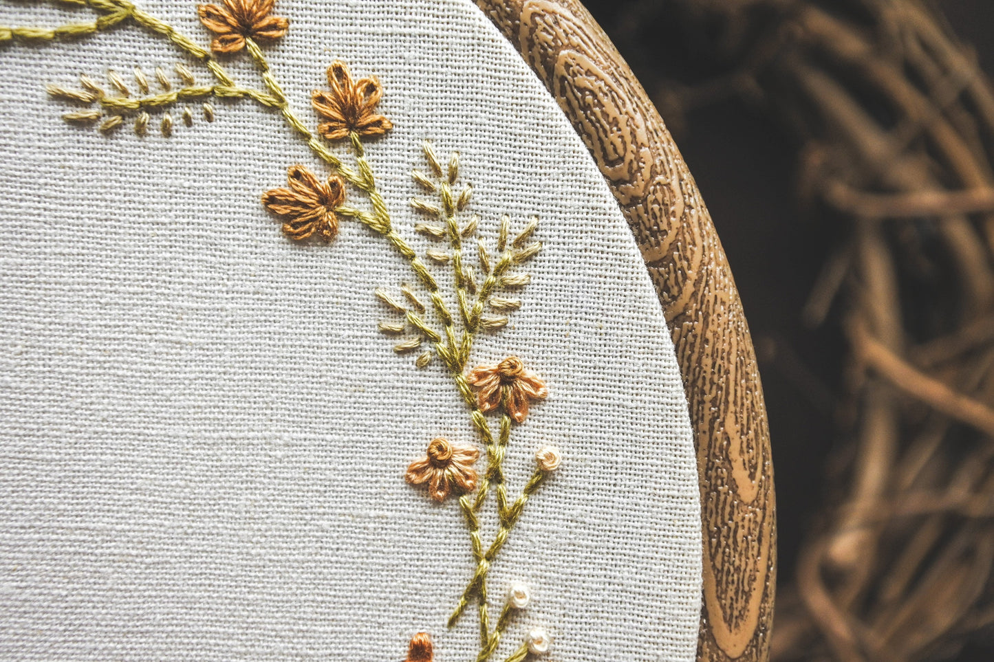 Close-up of hand-embroidered coneflowers, grasses, and leaves on autumn wreath embroidery hoop