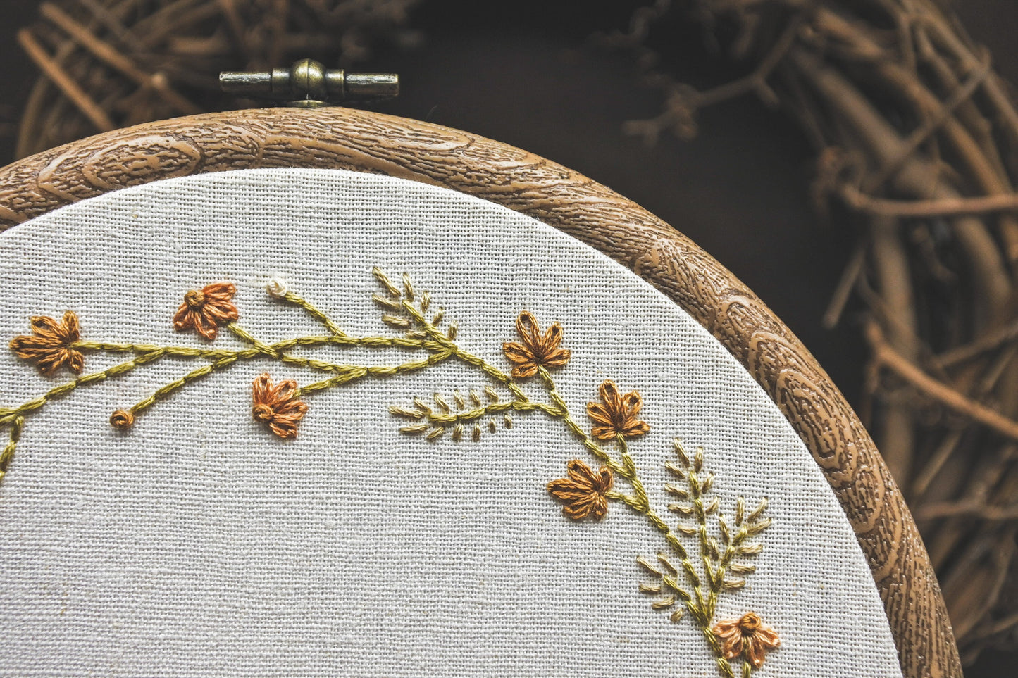 Close-up of hand-embroidered autumn wreath details, featuring leaves, grasses, and coneflowers