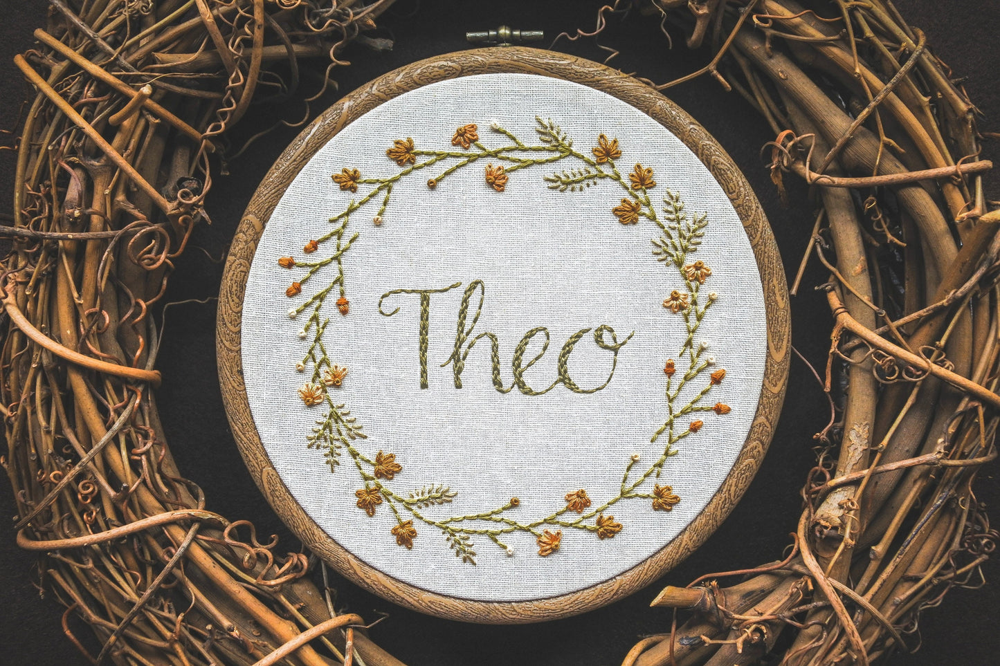Custom autumn wreath embroidery hoop with hand-embroidered name 'Theo' in the centre, surrounded by leaves, grasses, and acorns