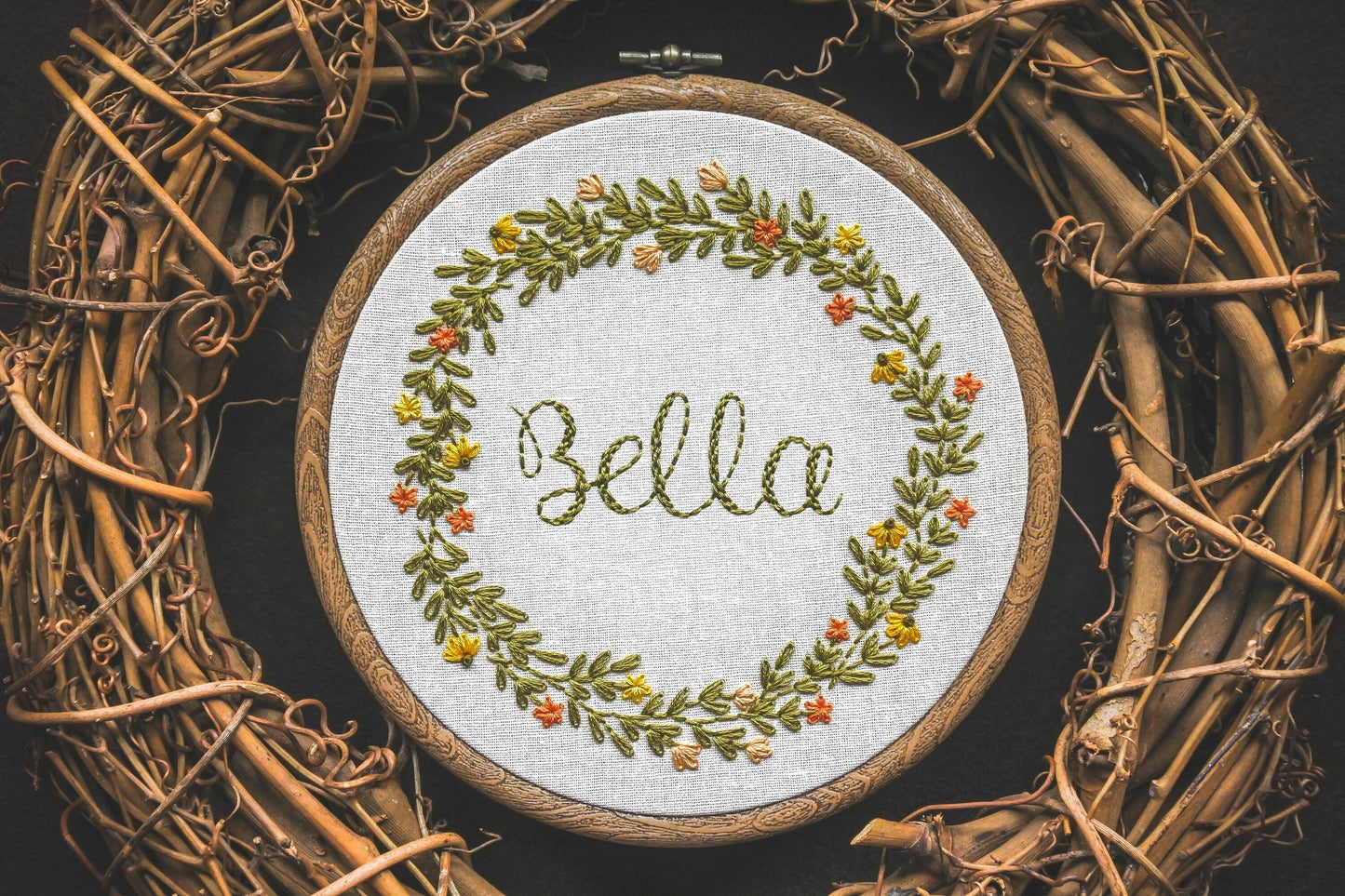 Hand embroidered summer wreath name hoop with the name Bella stitched in the centre, surrounded by orange and yellow flowers with lush greenery