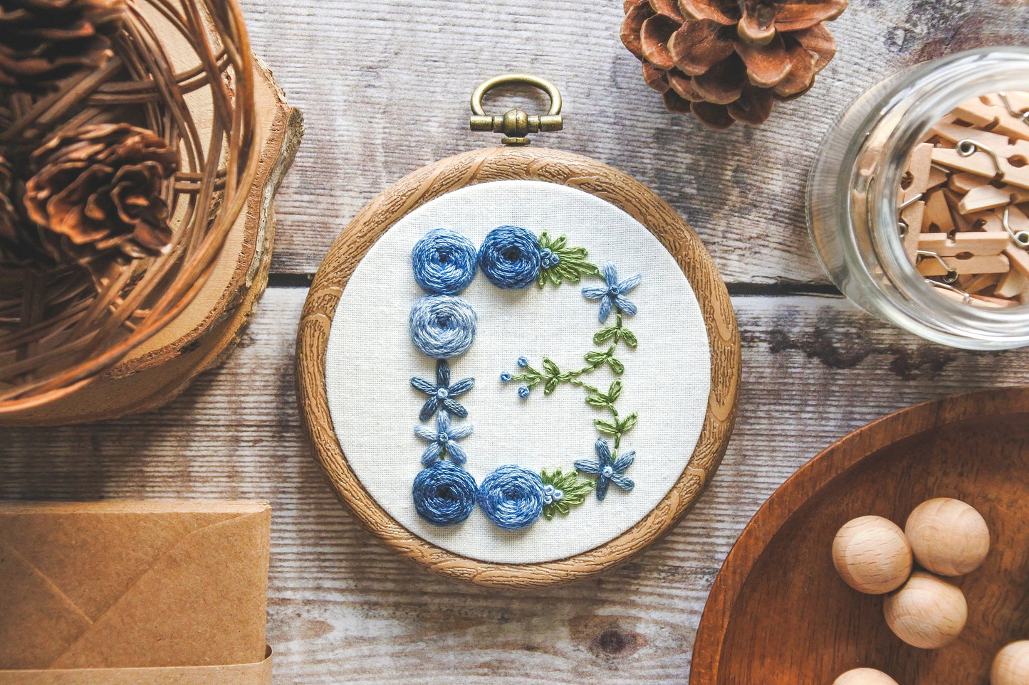 Blue floral 'B' hand-embroidered hoop with green foliage.
