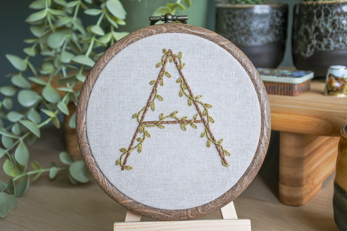Closeup of the hand-embroidered botanical letter 'A' hoop on a mini wooden easel.