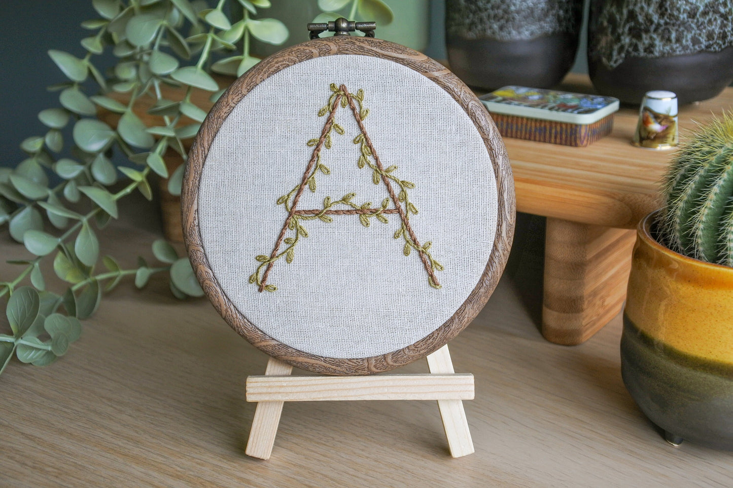 Hand-embroidered botanical letter 'A' hoop displayed on a mini wooden easel.