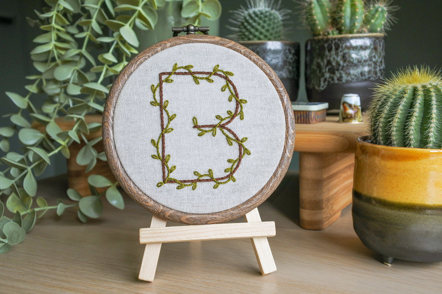 Hand embroidered letter b in a wood effect hoop displayed on a mini wooden easel.