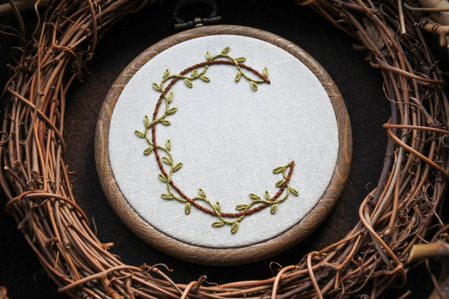 Botanical letter C embroidery hoop with green vines and brown stitched letter on neutral fabric