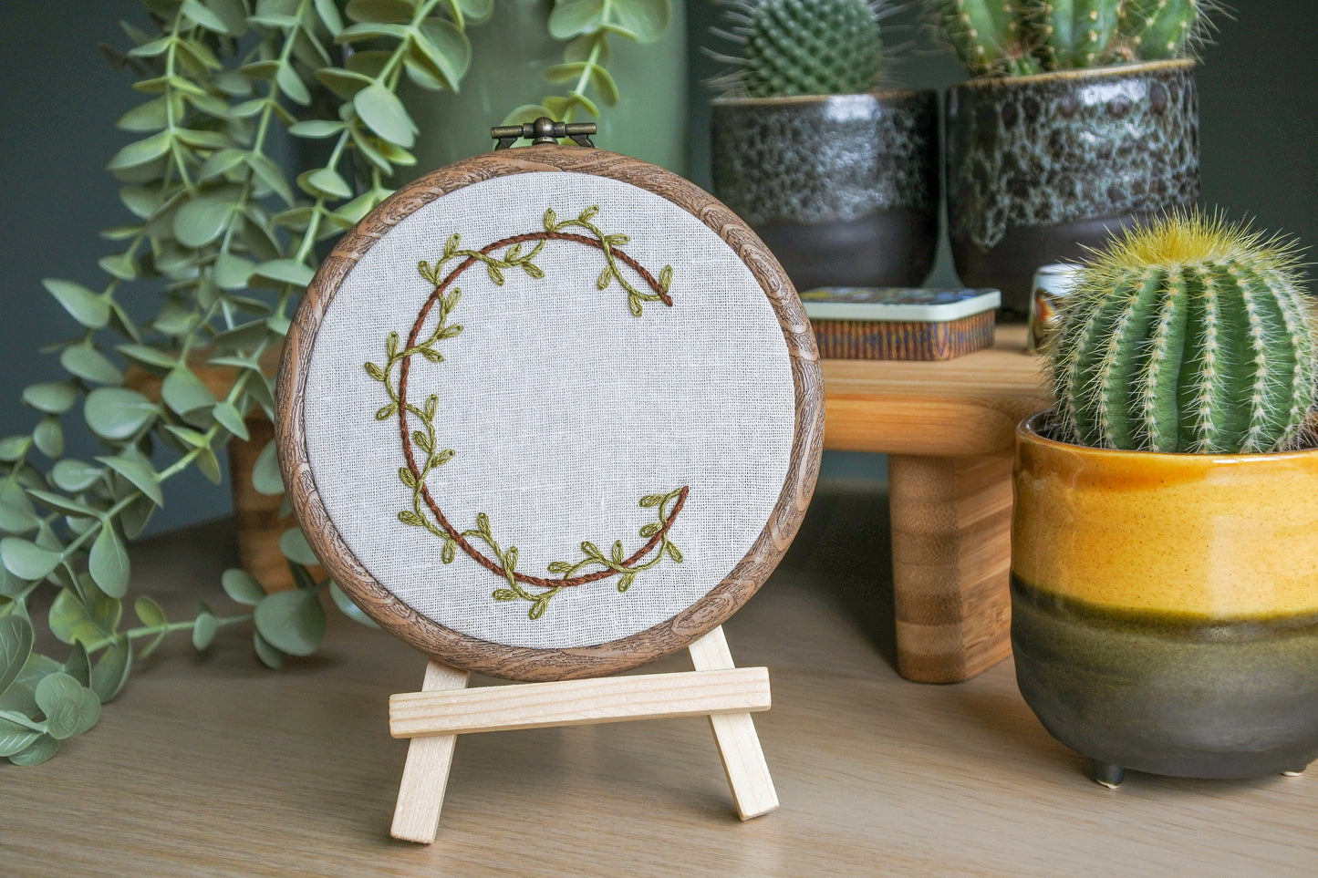 Botanical letter C embroidery hoop with green vines and brown letter displayed on a small wooden easel