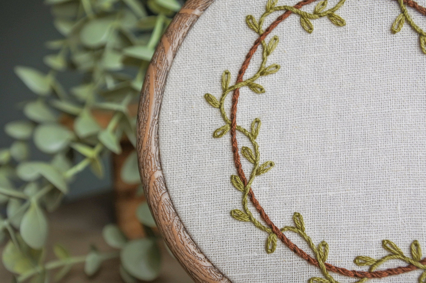 Close-up view of green leafy vine embroidery around the brown stitched letter C