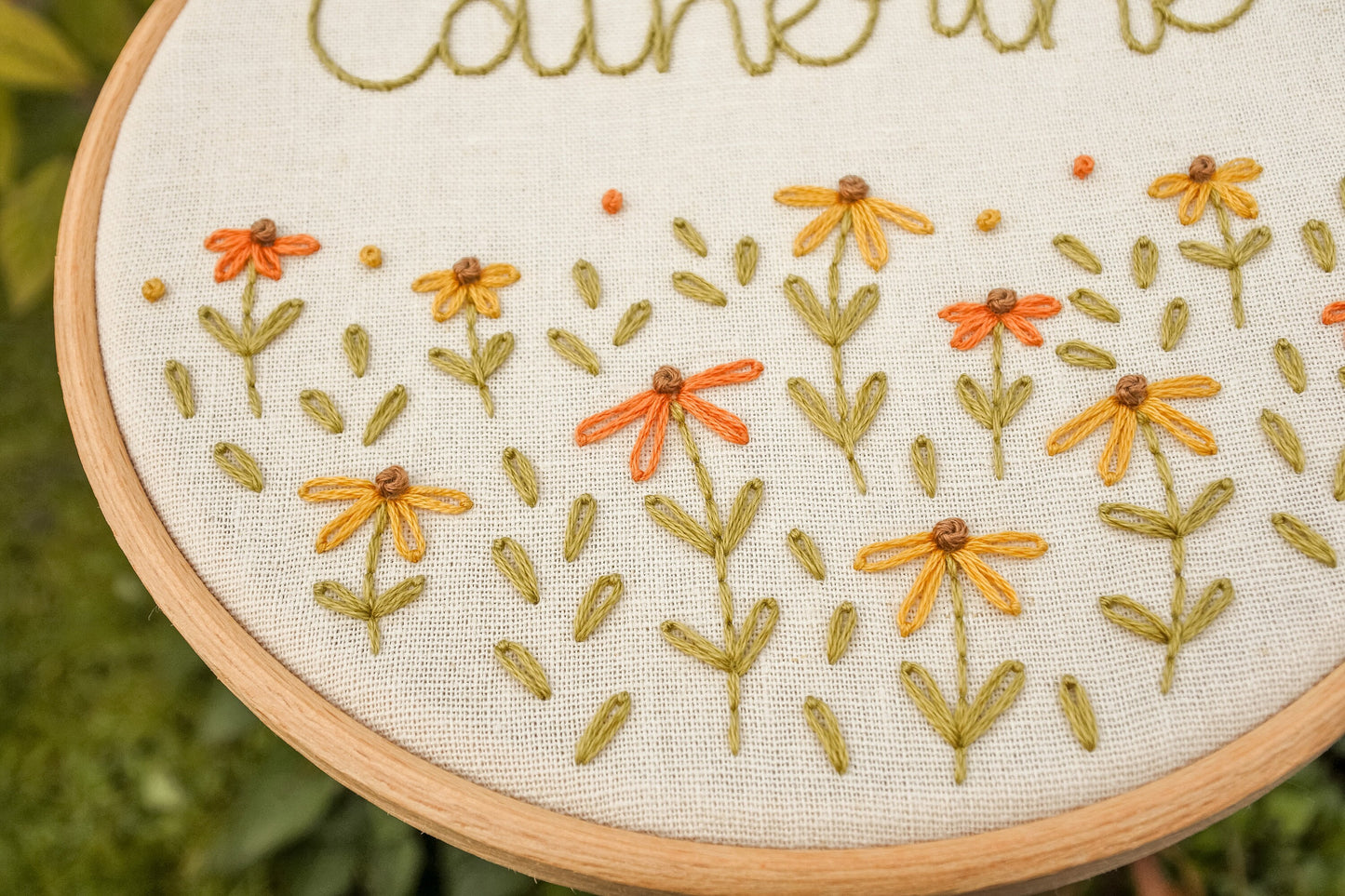 Close-up showing the stitching of the warm orange and mustard yellow coneflowers and warm green leaves on the personalised embroidery hoop.