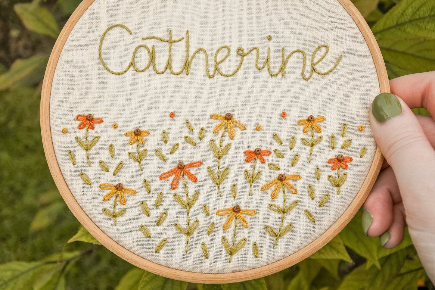 Close-up of the personalised coneflower name embroidery hoop, highlighting the name Catherine and the warm orange, mustard yellow, and green coneflower design.