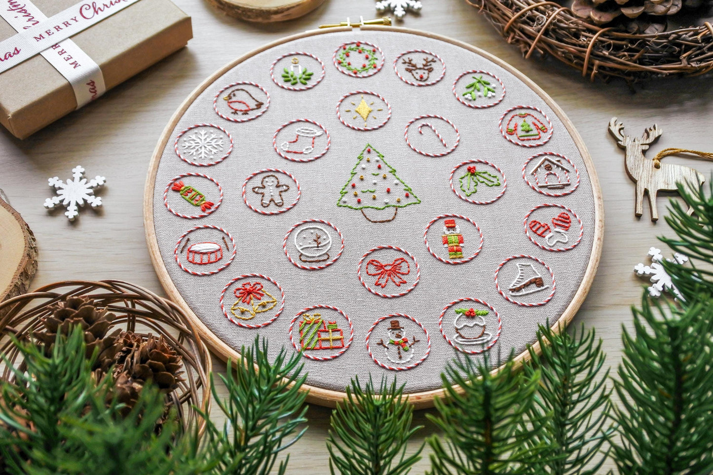Hand embroidered Christmas advent calendar hoop, photographed at a slight angle showing festive design details on beige fabric.