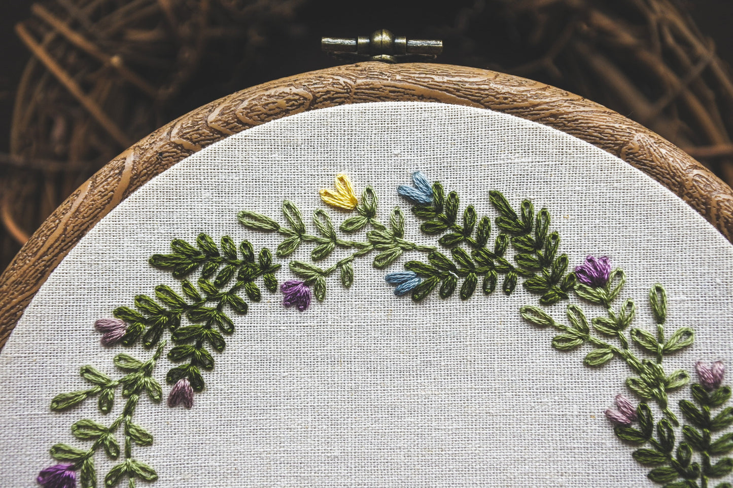Close-up of hand embroidered spring flowers in yellow, purple, and blue with green foliage on a light neutral background.