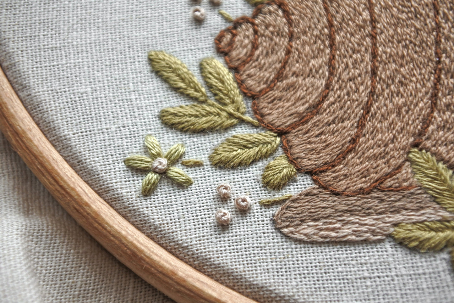 Closeup of embroidery details showing leaves and flower behind the snail's shell