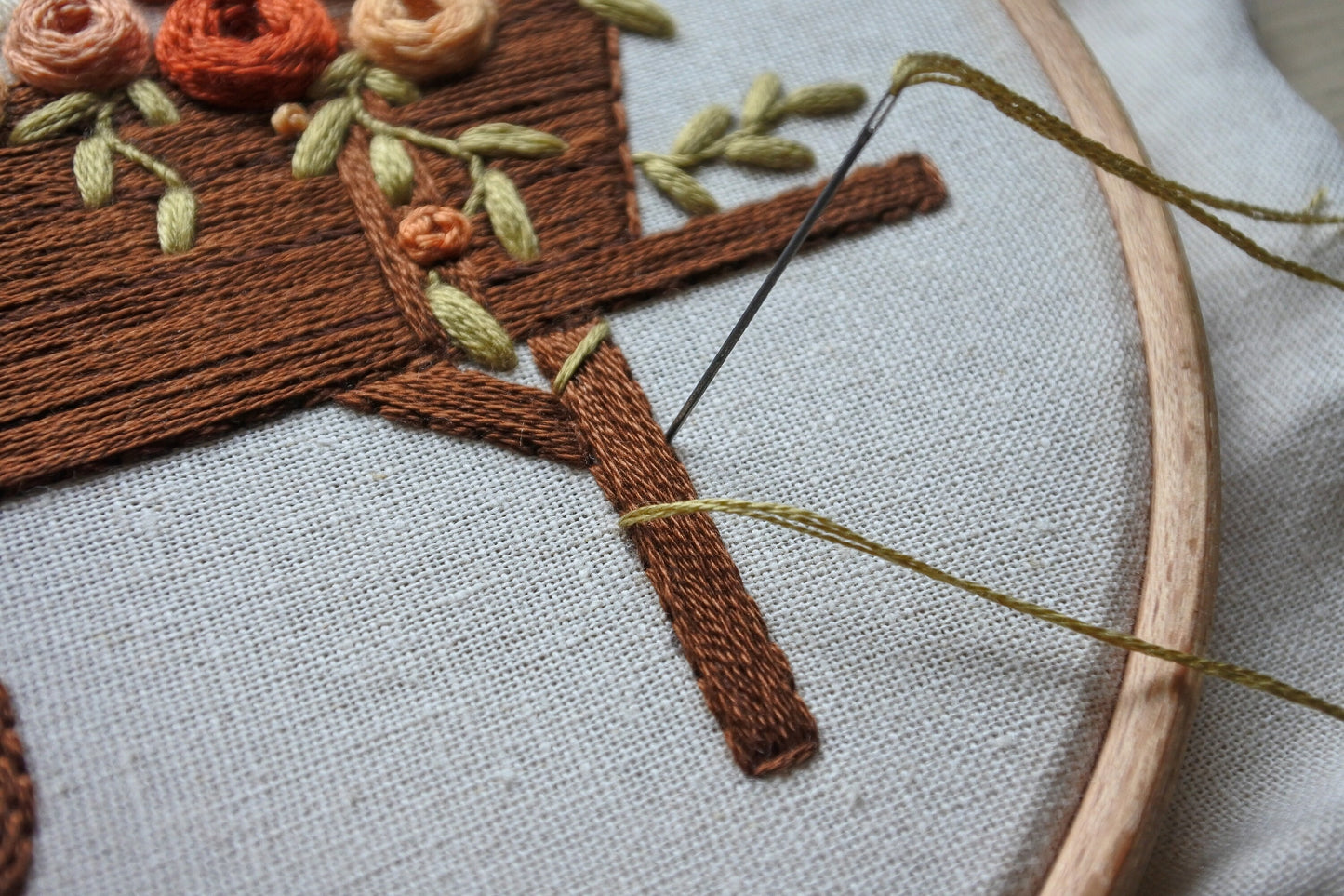 Close-up of needle and thread stitching the vine around the leg of the wagon on the autumn embroidery pattern