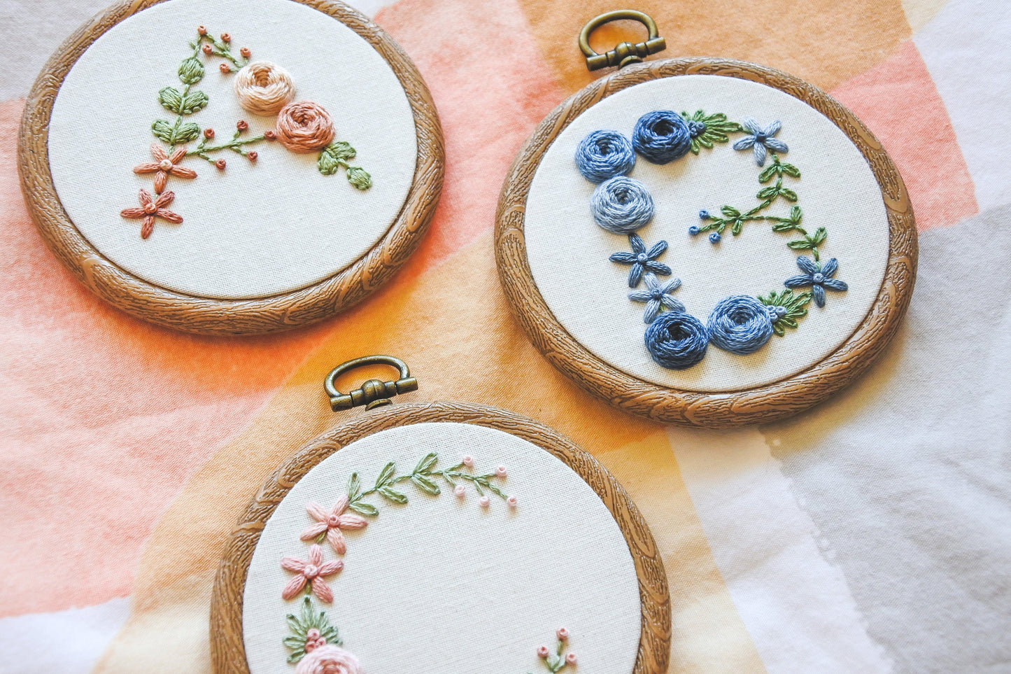Floral letter 'A', 'B', and 'C' hand-embroidered hoops photographed at an angle.