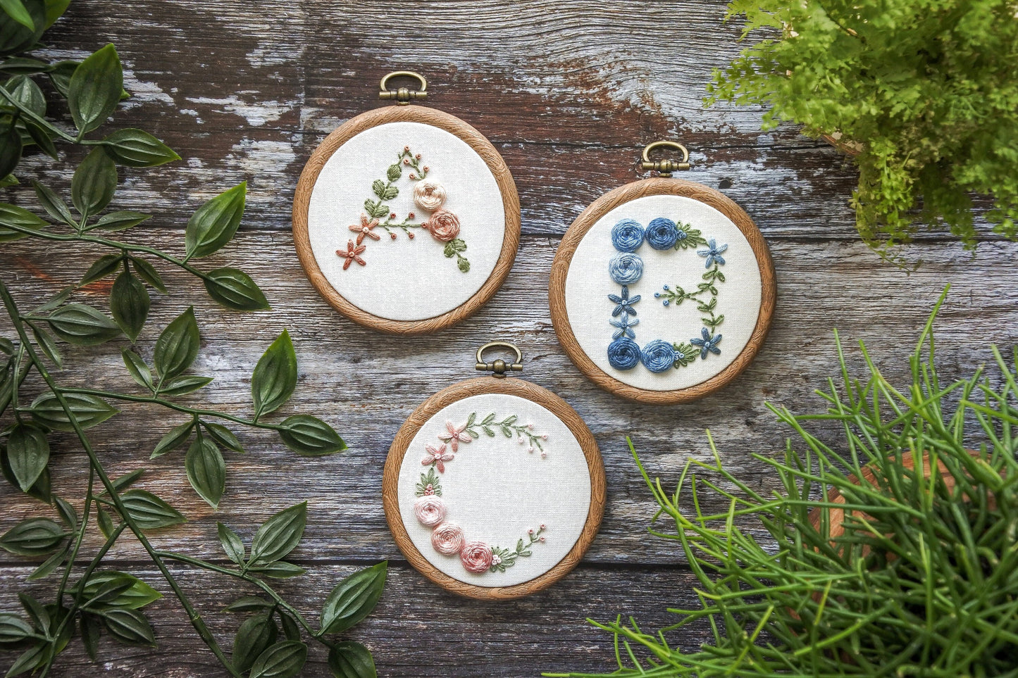 Floral letter A, B, and C embroidery hoops featuring peach, blue, and pink flowers with green foliage.