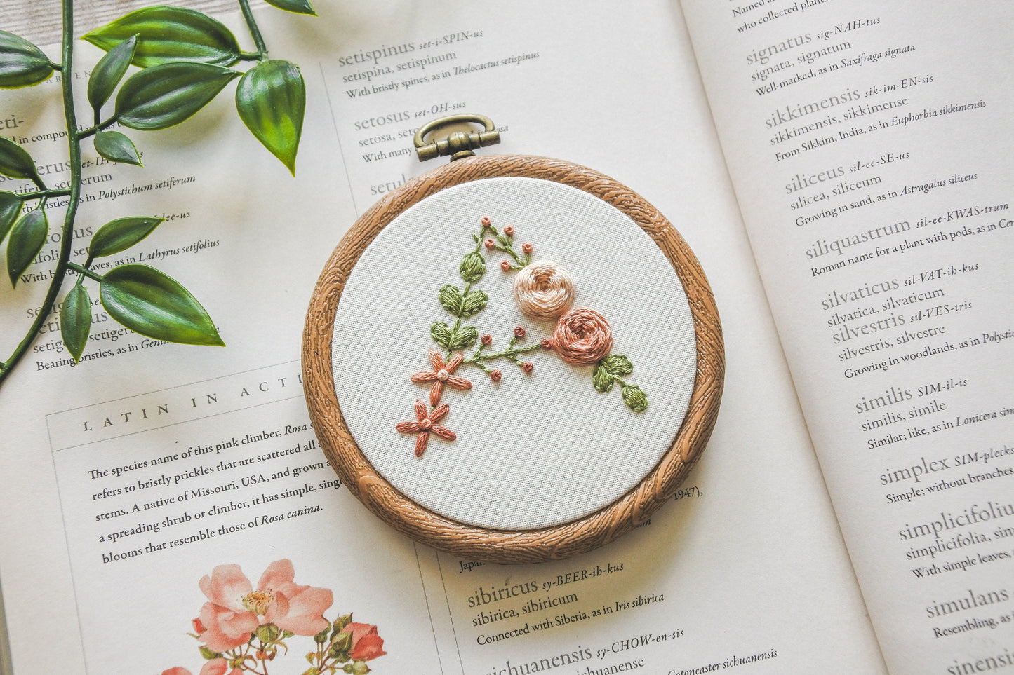 Hand-embroidered floral letter A hoop featuring peach flowers and green foliage in a 3-inch wood-effect hoop.