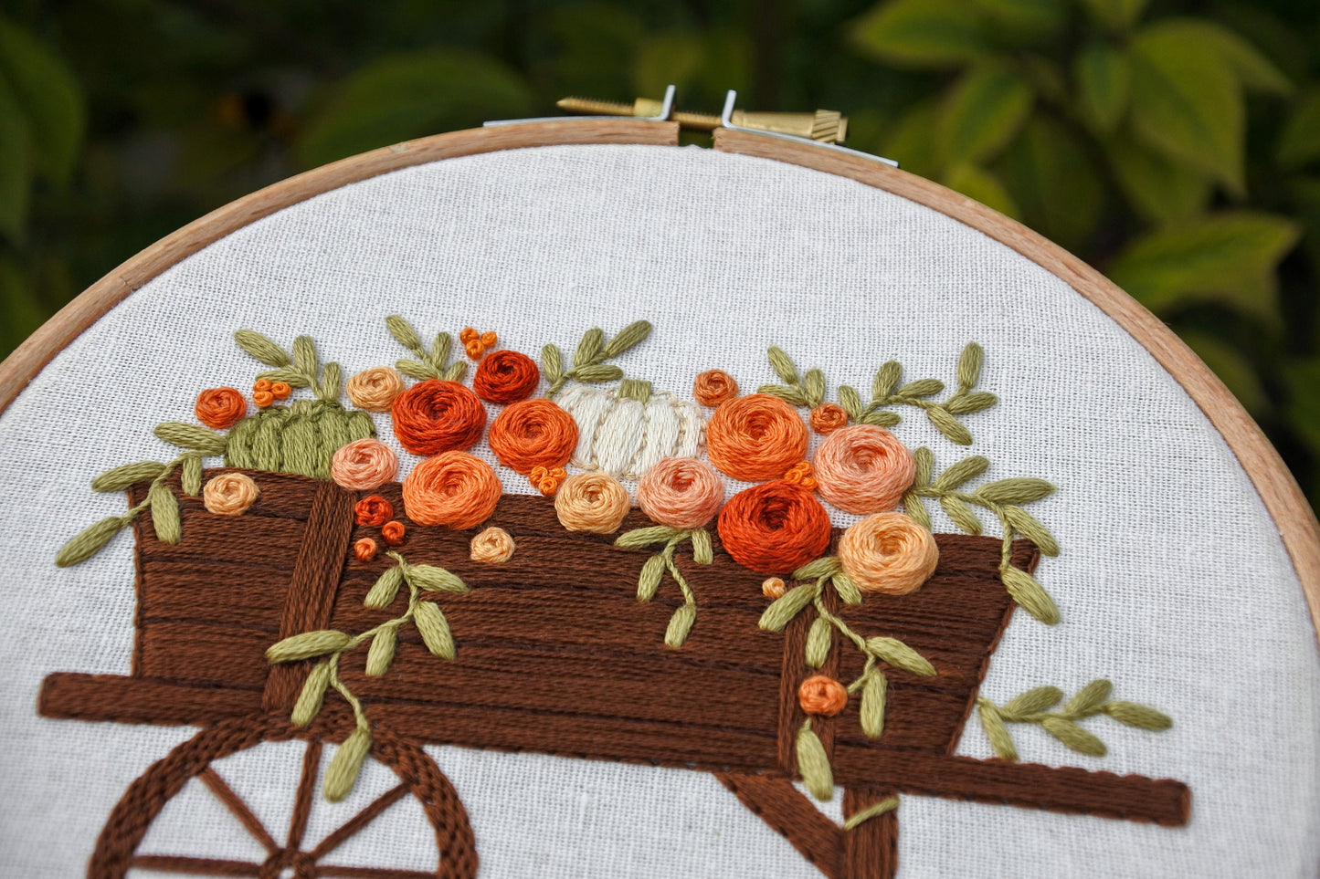 Closeup of the hand embroidered pumpkins, flowers and foliage in the brown wagon.