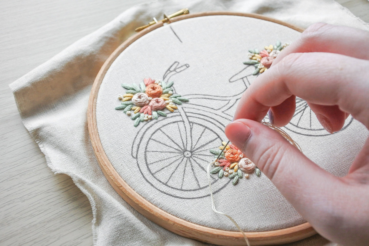 Close-up of a French knot being stitched on the floral bicycle design.