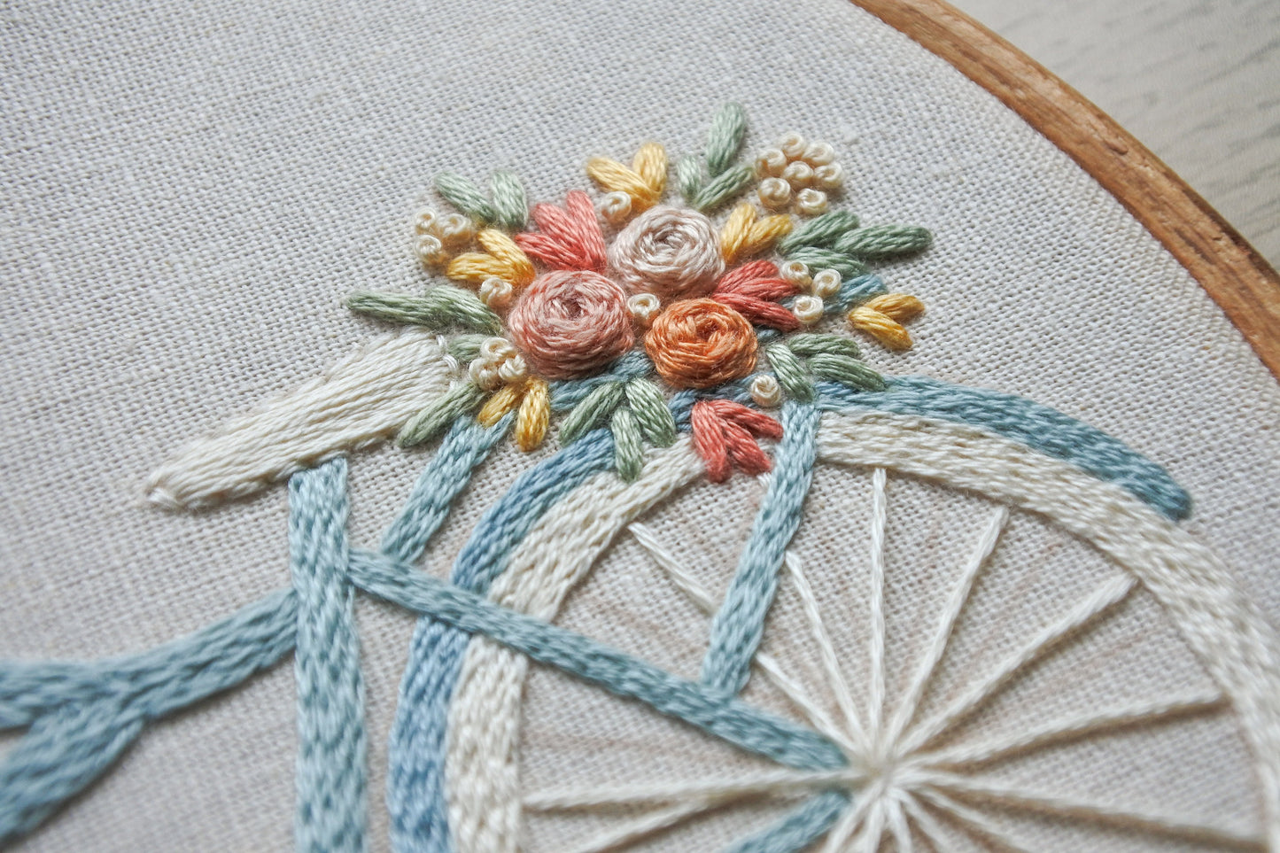 hand embroidered floral bouquet in pastel colours including pink, yellow and orange with green leaves on the back of a blue and white bicycle.
