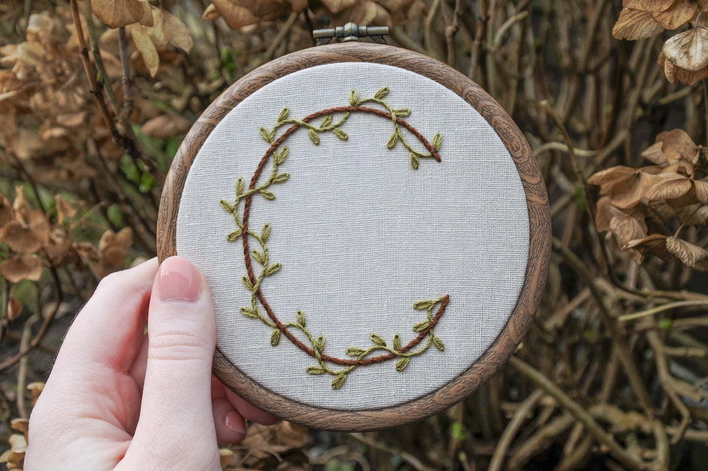 Hand holding botanical letter c embroidery hoop art