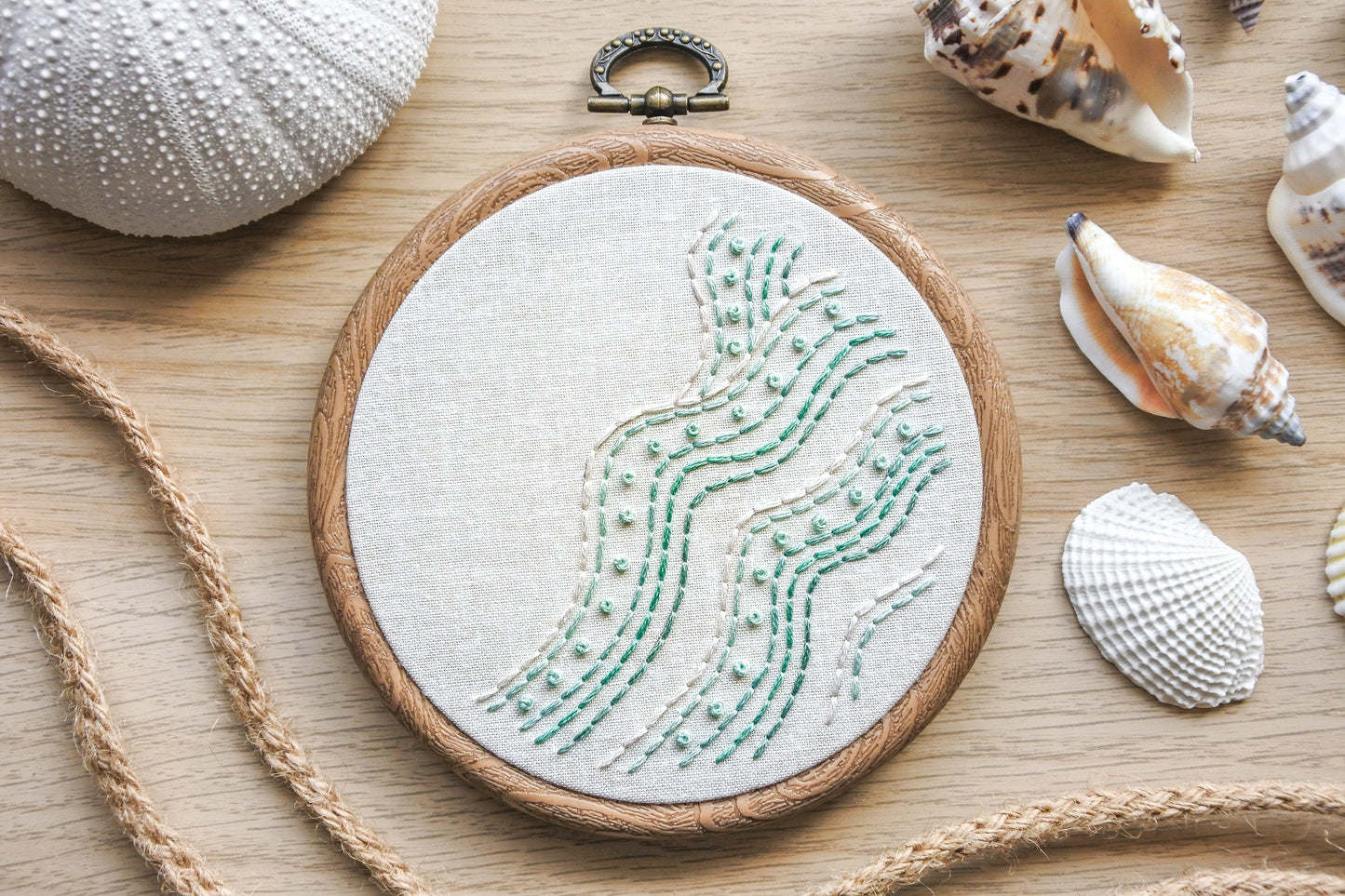 Minimalist beach wave embroidery hoop with turquoise and white stitches, featuring backstitch and French knots