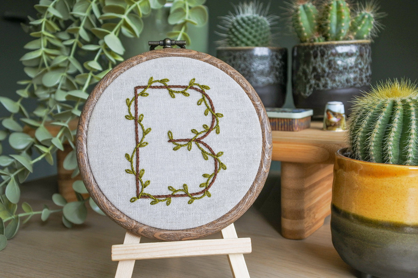 Hand embroidery hoop with botanical letter B design stood on a mini wooden easel.