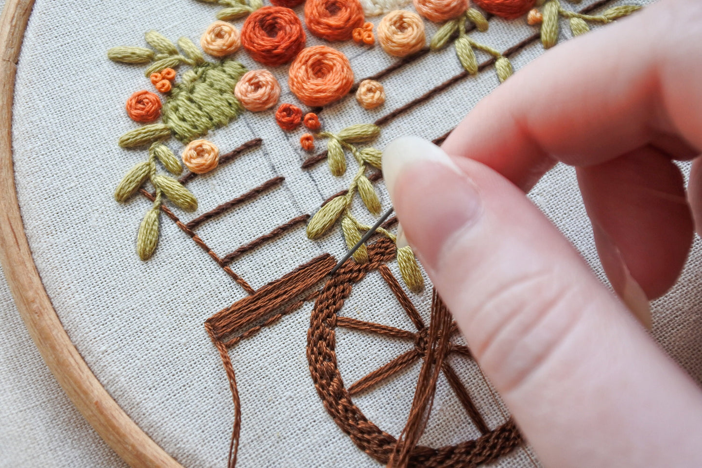 Hand stitching the wagon on an autumn floral embroidery pattern, showing the progress of the design