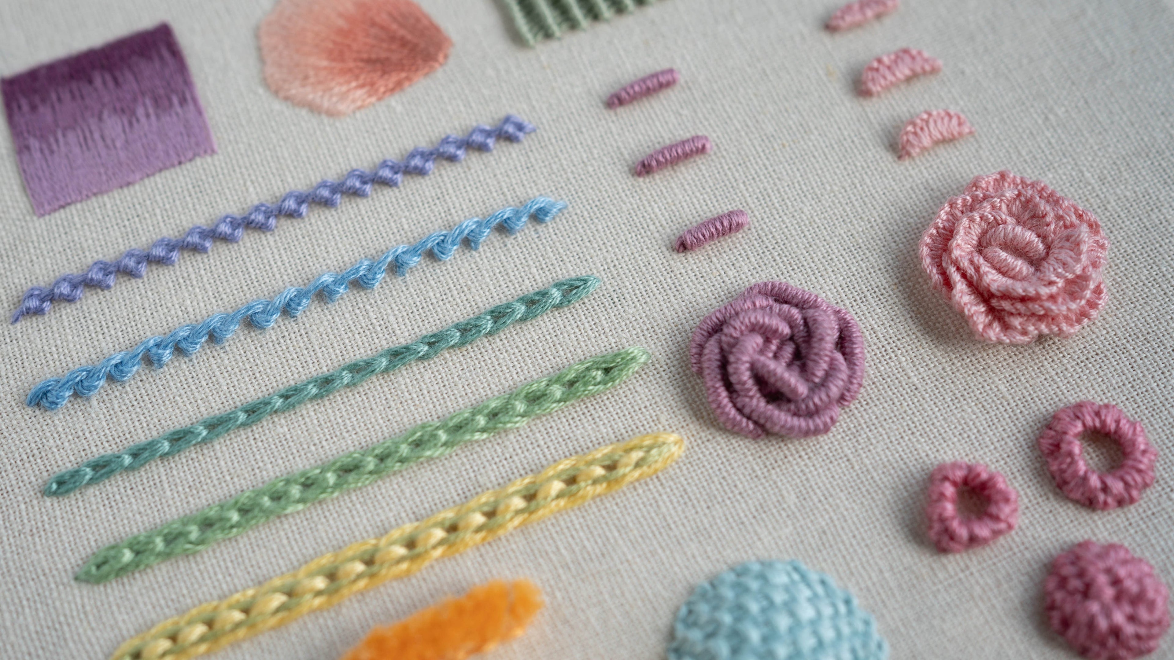 closeup angled photo of a hand embroidery stitch sampler featuring various stitches in bright pastel colours