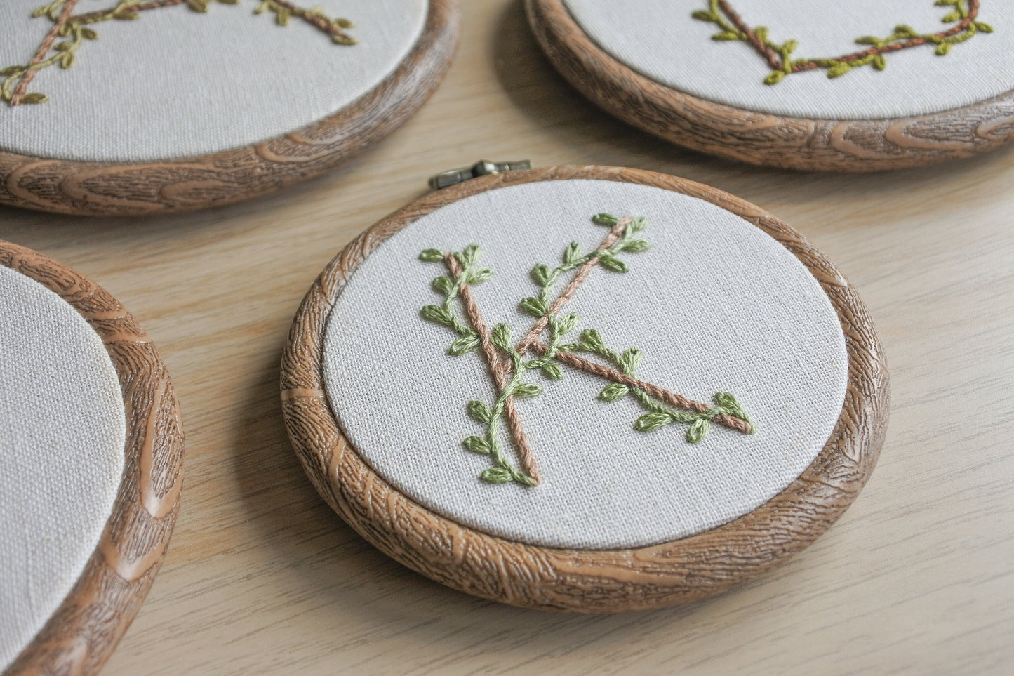 side angle view of the letter k embroidery hoop art details, with pale brown letter and eucalyptus green vines