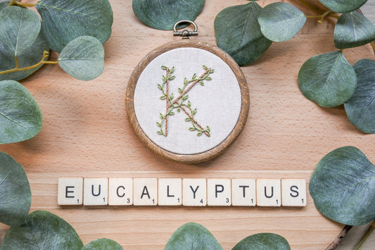 Hand embroidered letter K hoop with eucalyptus leaves and 'eucalyptus' spelled in wooden scrabble tiles