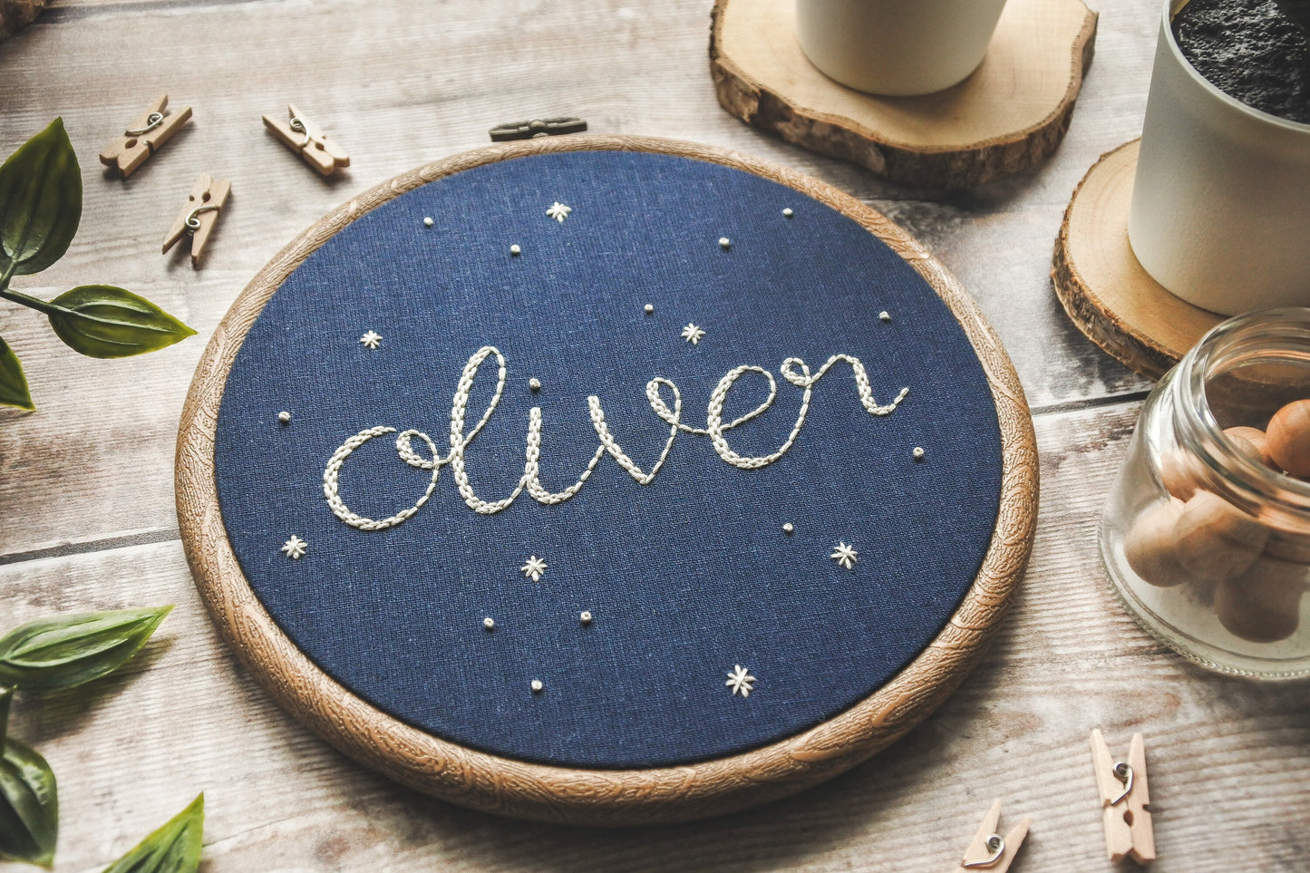 Angled photo of hand embroidered 'Oliver' name hoop with white stars on dark navy fabric in a wood-effect hoop