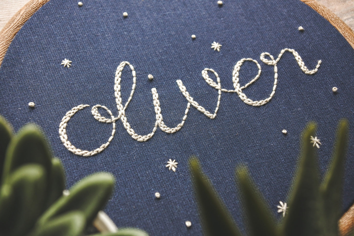 Close up view of hand embroidered name 'Oliver' stitched in white thread on navy blue fabric with surrounding stars