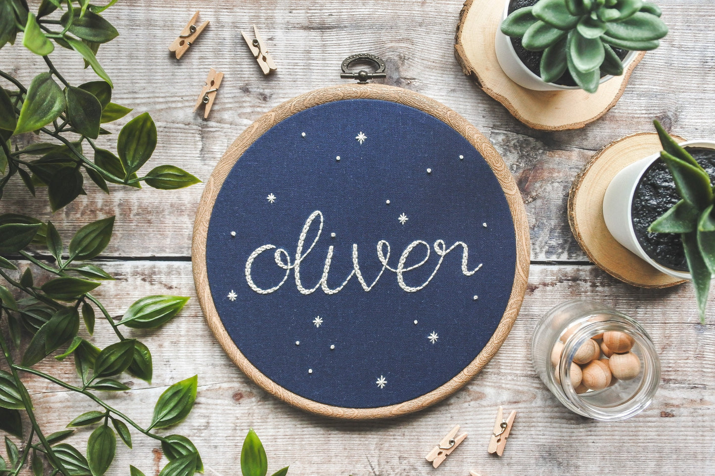 Starry name embroidery hoop with 'Oliver' stitched in white thread and surrounded by stars on navy blue fabric