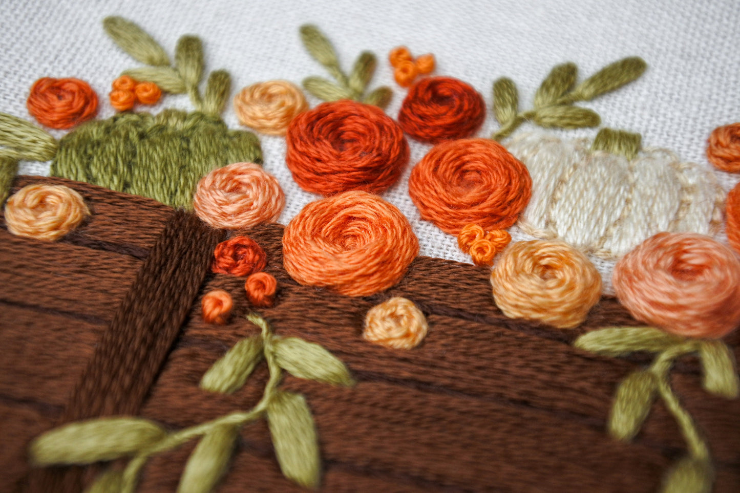 closeup of the hand embroidered orange, red and peach rose flowers in the autumn wagon design.