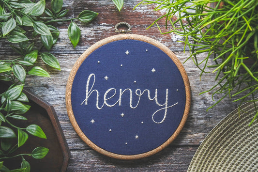 Hand embroidered name hoop featuring the name Henry stitched in white thread on navy fabric, displayed flat