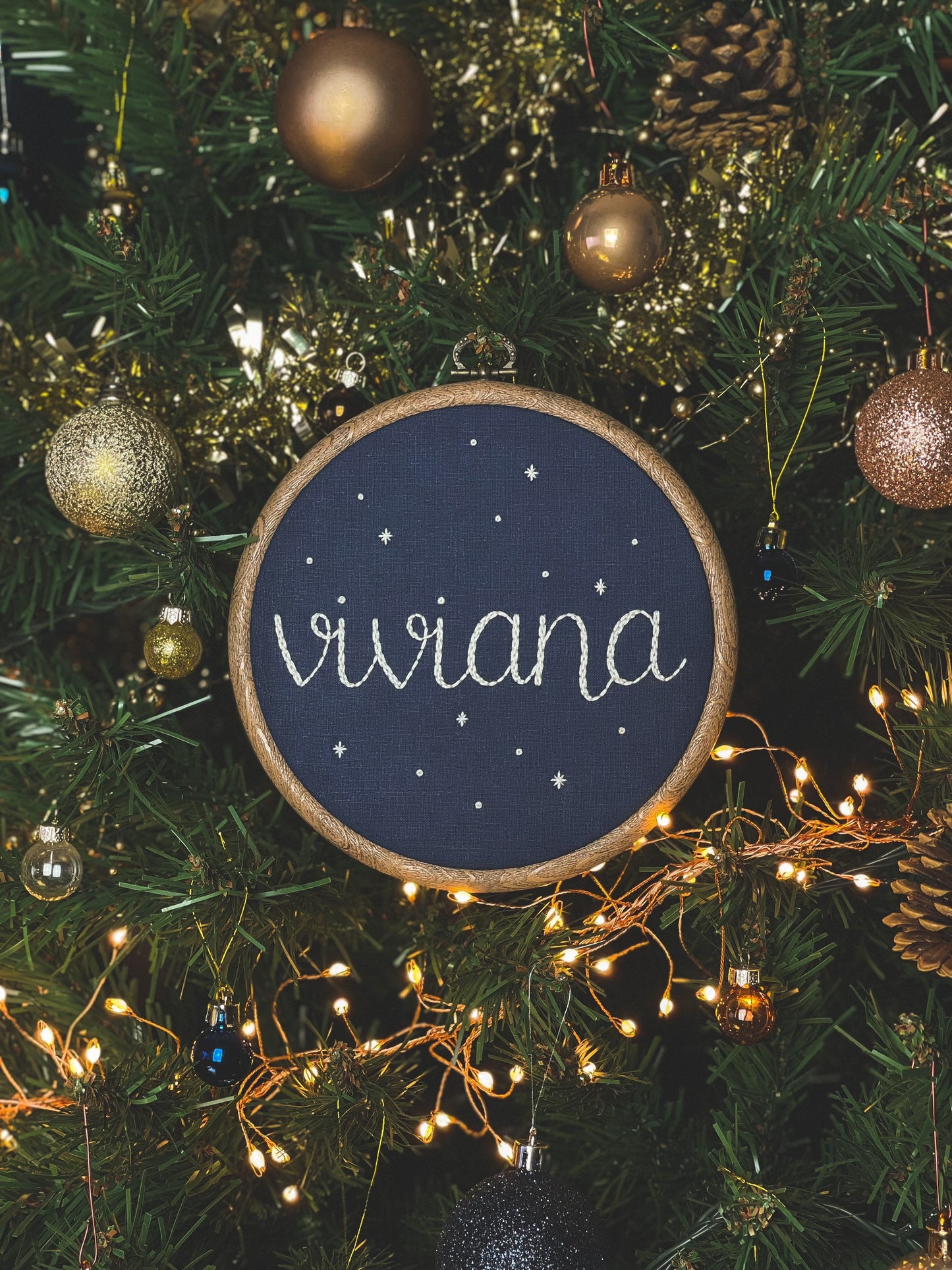Viviana starry name hoop hanging on a Christmas tree branch, surrounded by warm festive lights and ornaments