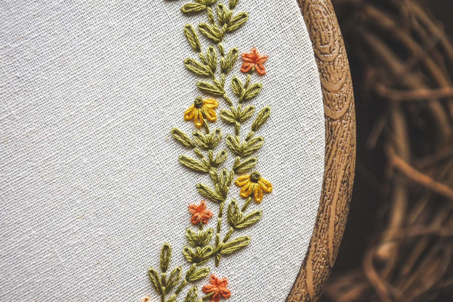 Closeup of the embroidered summer wreath showing yellow and orange flowers with hand stitched greenery