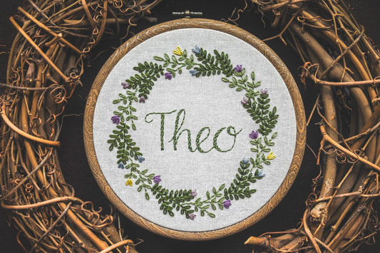 Hand embroidered spring wreath name hoop with the name Theo stitched in the centre, featuring fresh floral details and greenery