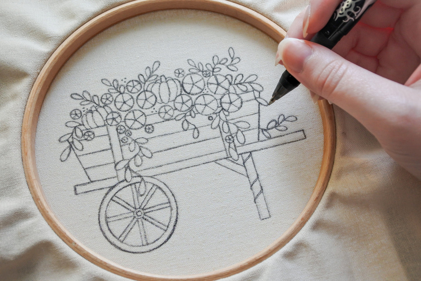 Hand holding a pen while transferring an autumn wagon embroidery pattern onto fabric