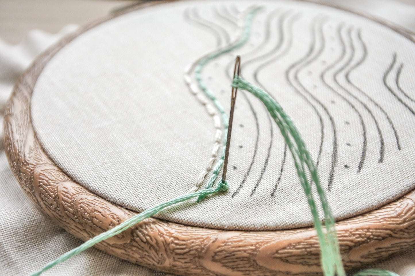 Closeup of a needle stitching a turquoise French knot on the beach wave embroidery pattern