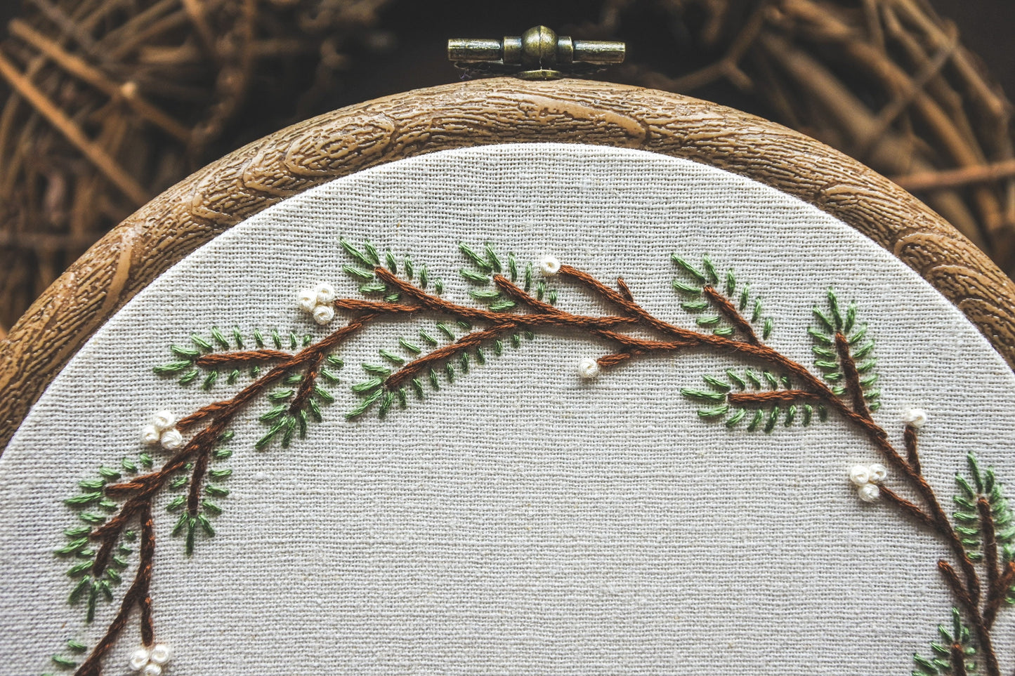 Detail of embroidered pine branches and white berries in a winter-themed hoop