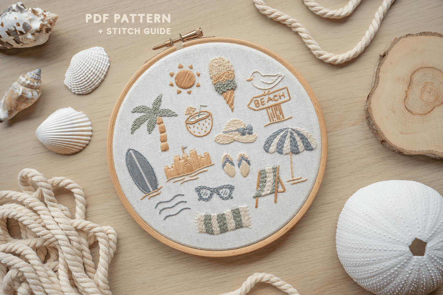 Embroidery hoop with beach-themed designs surrounded by seashells and rope on a wooden surface