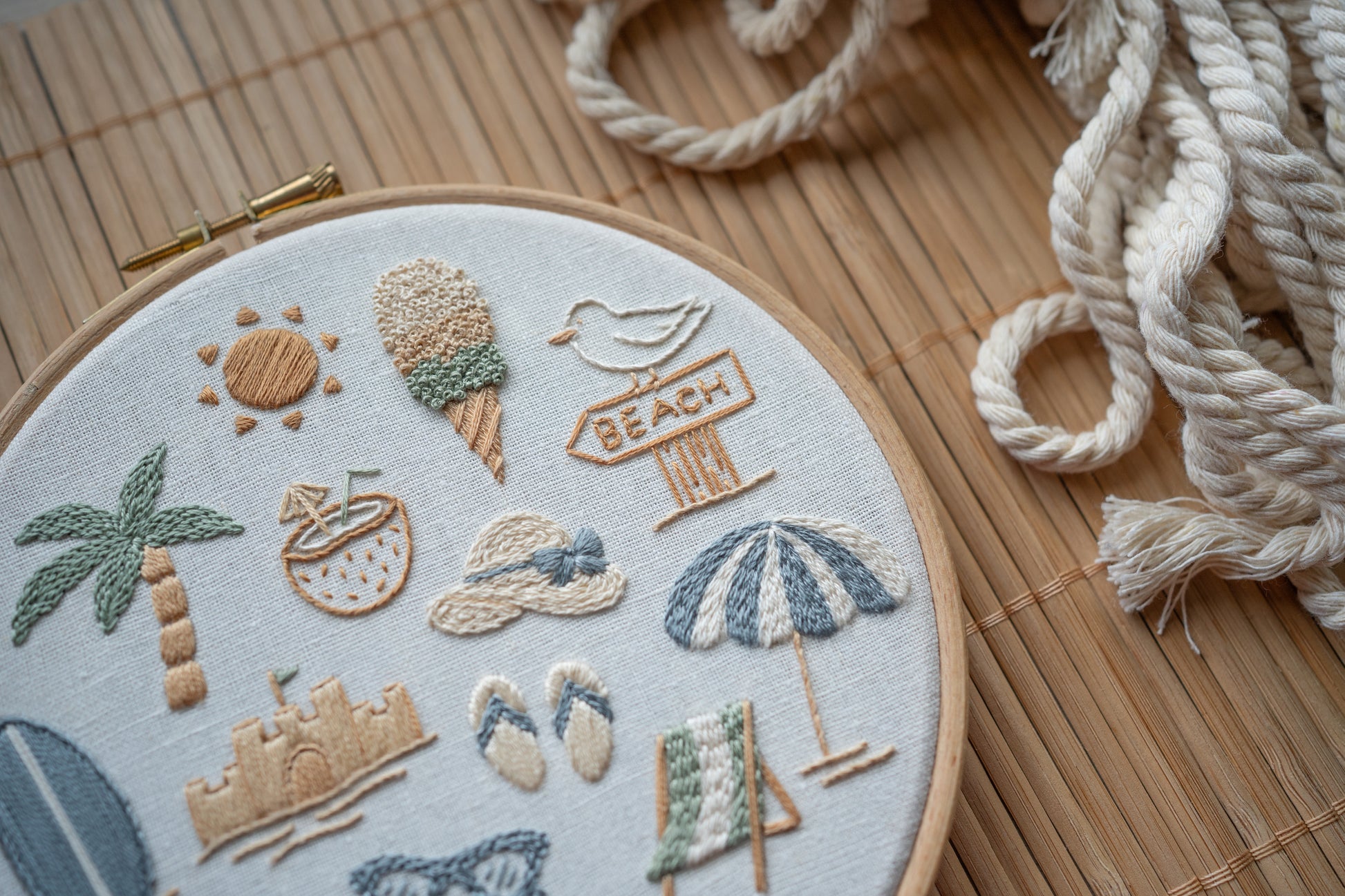 Embroidery hoop with beach-themed designs on a wooden surface with rope.