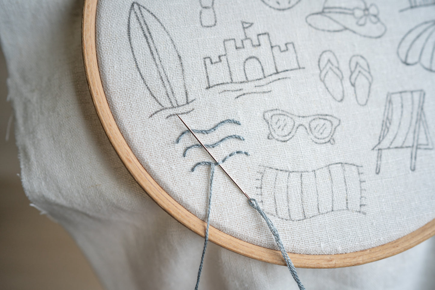 Embroidery hoop with a partially completed design of Ocean waves by the beach.