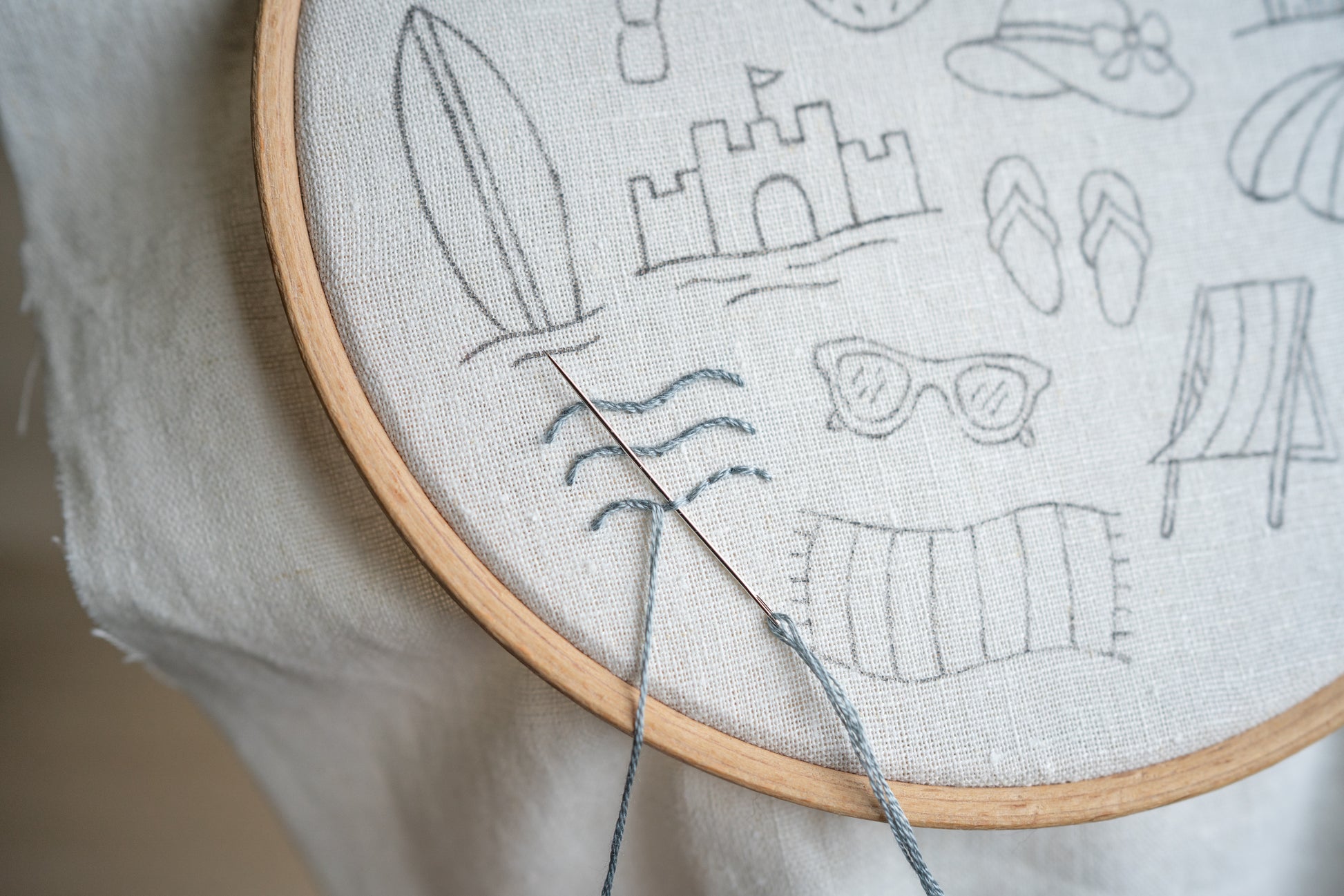 Embroidery hoop with a partially completed design of Ocean waves by the beach.
