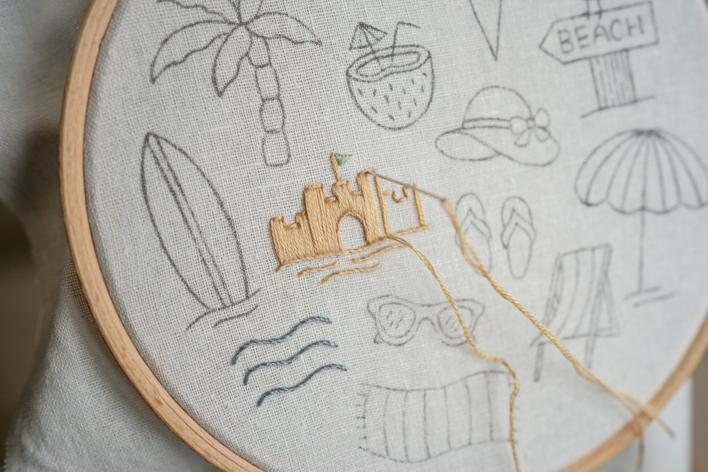 Embroidery hoop with beach-themed embroidery including a sandcastle, palm trees, and surfboard.