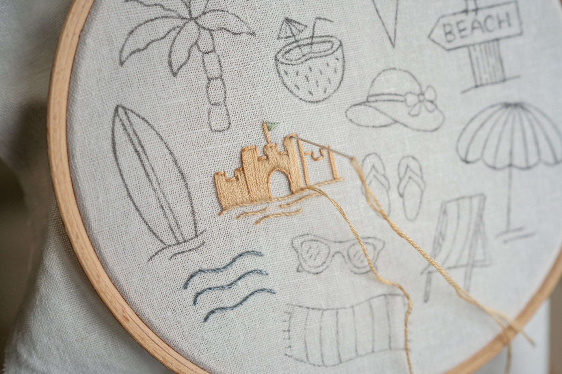 Embroidery hoop with beach-themed embroidery including a sandcastle, palm trees, and surfboard.